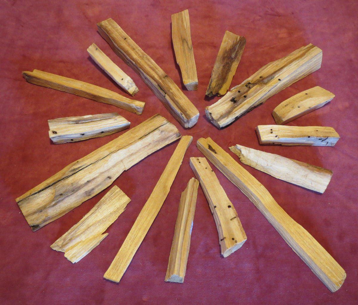 Palo Santo Stücke in unterschiedlichen Größen auf einem bordeaux roten Tuch