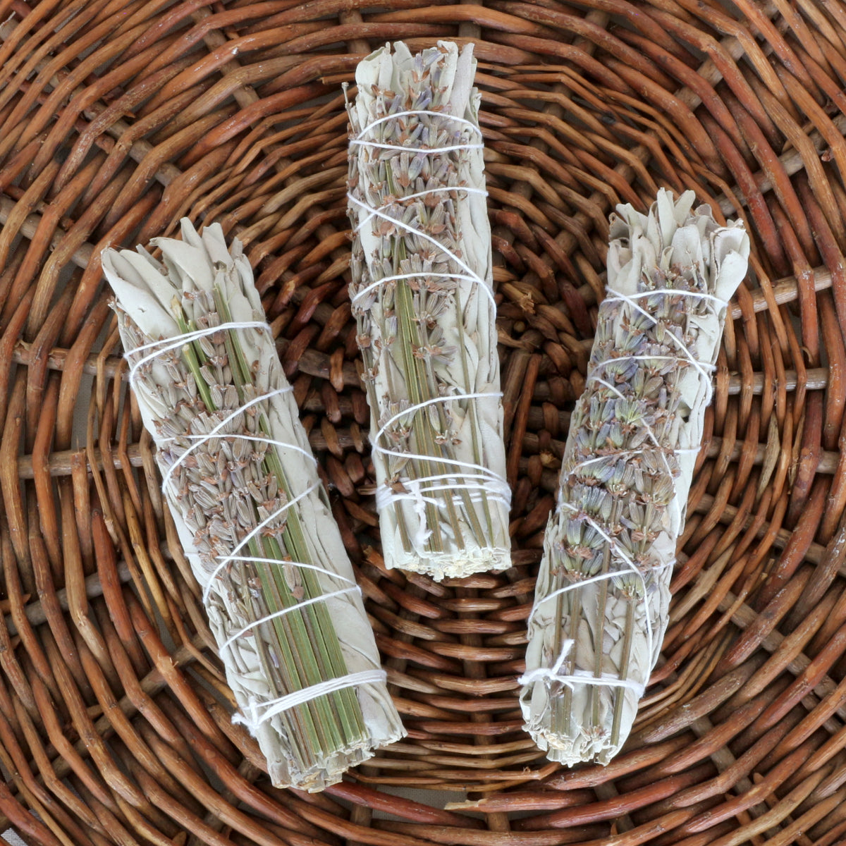 Drei kleine handgebundene Salbei-Lavendel Räucherbündel – Smudge Sticks zur energetischen Reinigung auf einem geflochtenen Weidenteller